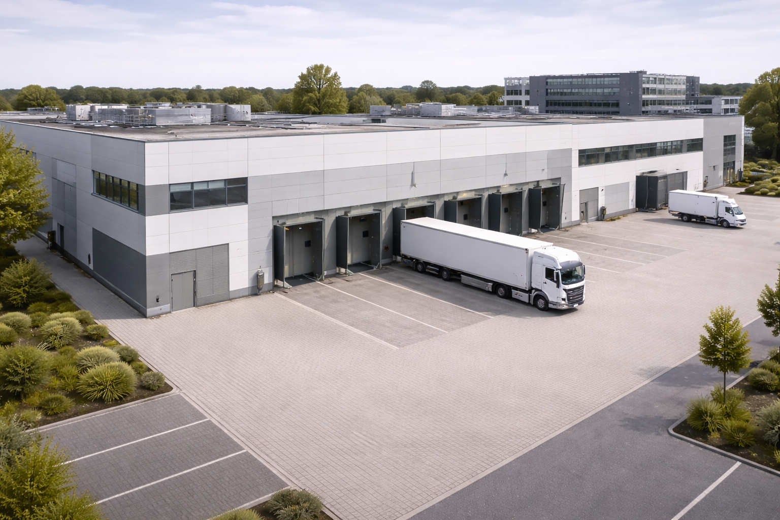 Industrial logistics warehouse with multiple dock doors and two large white trucks parked at loading bays.